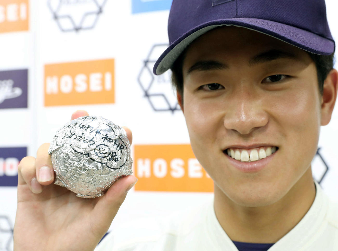 法大対明大　前日28日が誕生日の明大・木本は、決勝本塁打の記念球のカバーに仲間からメッセージを寄せられて笑顔を見せる（撮影・松本俊）