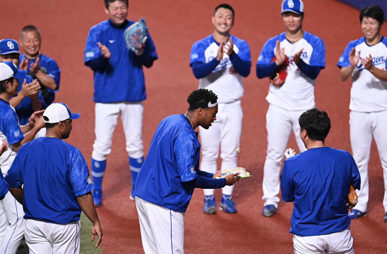 試合前練習の合間に投手陣からNPB通算100セーブ達成を祝い贈られたケーキを手にするマルティネス（中央）（撮影・森本幸一）