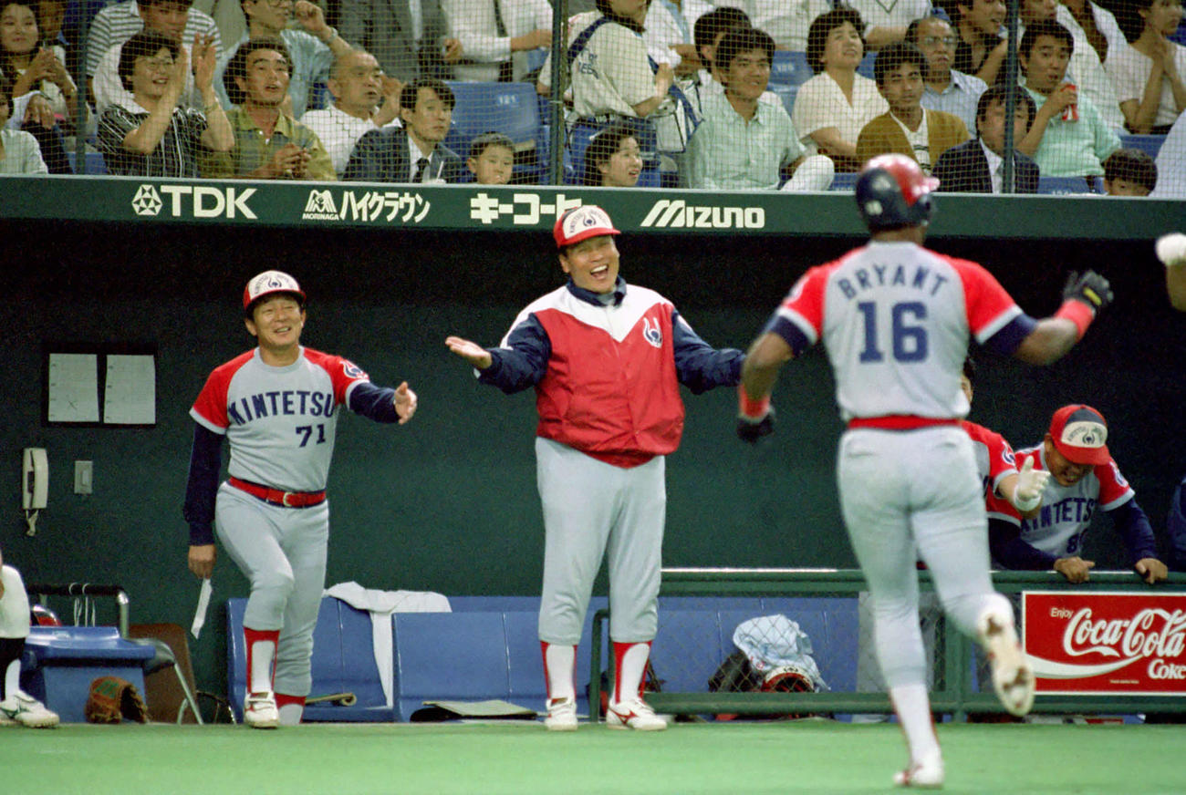 1990年6月6日、日本ハム対近鉄　ブライアント（右）が東京ドームの天井からつるされたスピーカーを直撃する認定本塁打を放ち、ベンチ前で出迎える中西コーチ（中央）も驚いたような笑顔を見せた。左は仰木監督