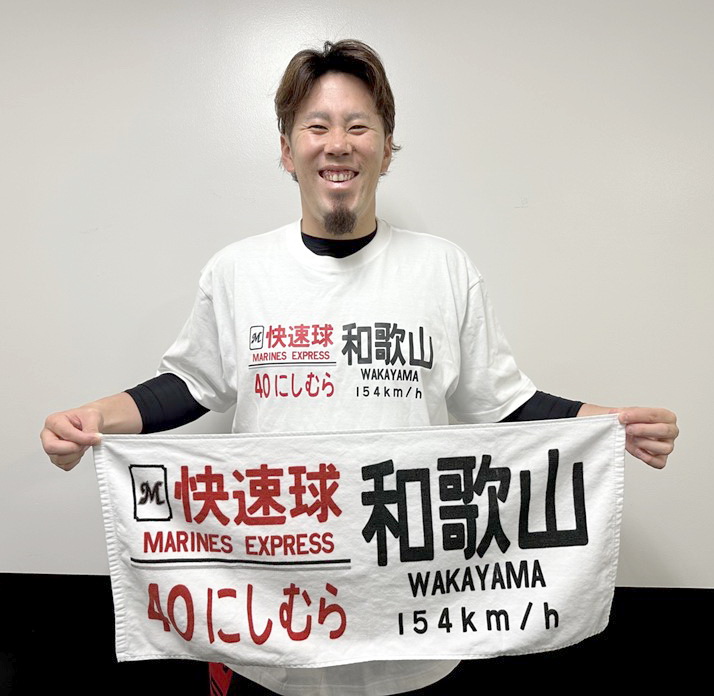 「西村快速球グッズ」のTシャツを着て、笑顔でフェースタオルを持つロッテ西村（球団提供）