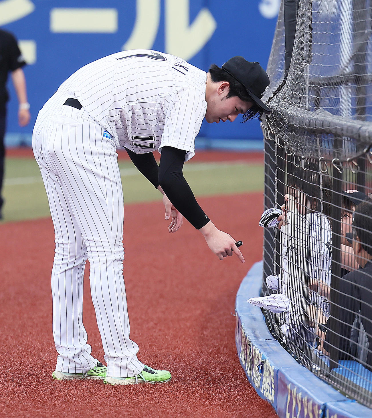 ロッテ対広島　試合後、ファンのこどものユニホームを網の隙間から取り出しサインするロッテ佐々木朗（撮影・足立雅史）