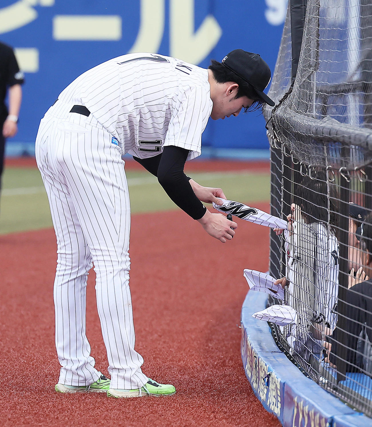 ロッテ対広島　試合後、ファンのこどものユニホームを網の隙間から取り出しサインするロッテ佐々木朗（撮影・足立雅史）