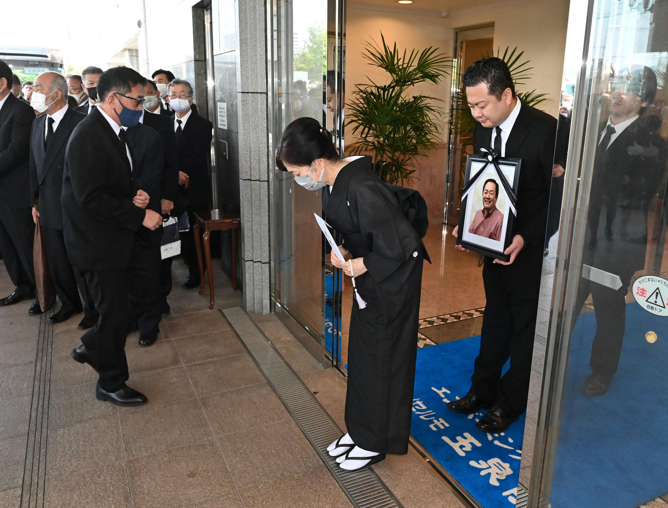北別府学氏告別式　妻の広美さん（中央）と遺影を手にする長男の大さん