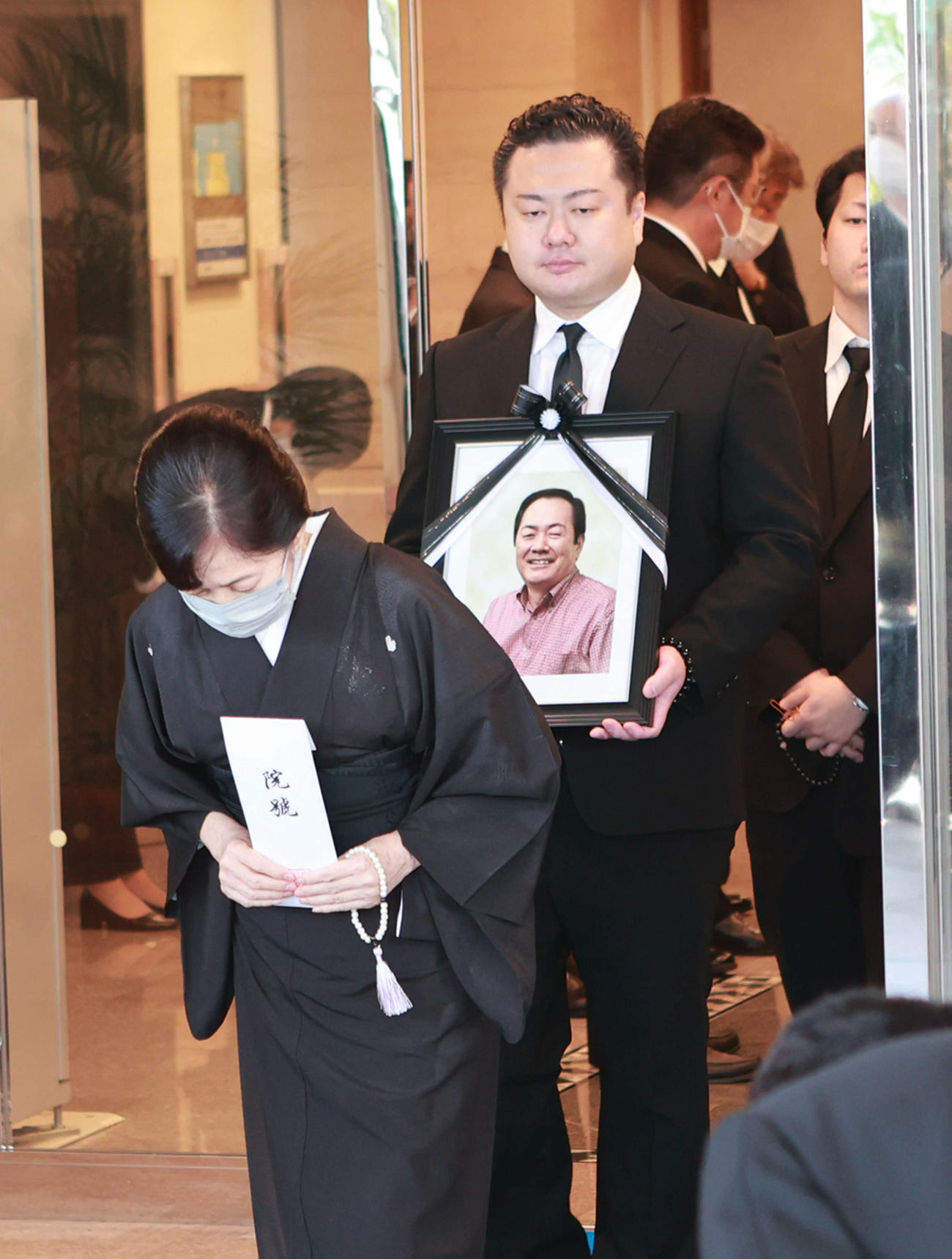 北別府学氏告別式　出棺　妻の広美さんと遺影を持つ長男の大さん
