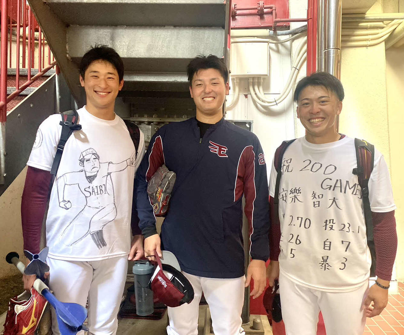 手書きのTシャツでプロ通算200登板を祝われ、笑顔の安楽智大投手（中央）と、左は内星龍、右は伊藤茉