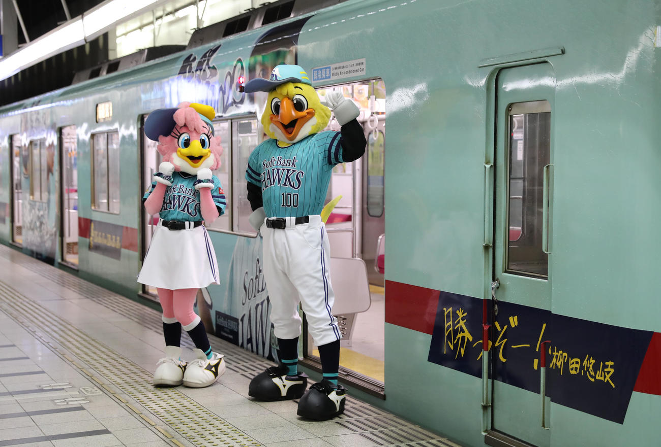 鷹の祭典2023特別デザインの西鉄ラッピング電車「勝つぞー！電車」と記念撮影に納まるハリーホーク(右)とハニーホーク(撮影・冨田成美)