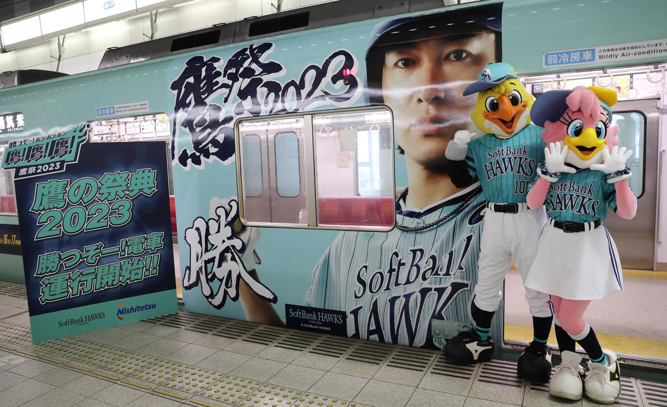 鷹の祭典2023特別デザインの西鉄ラッピング電車「勝つぞー！電車」と記念撮影に納まるハリーホーク(左)とハニーホーク(撮影・冨田成美)