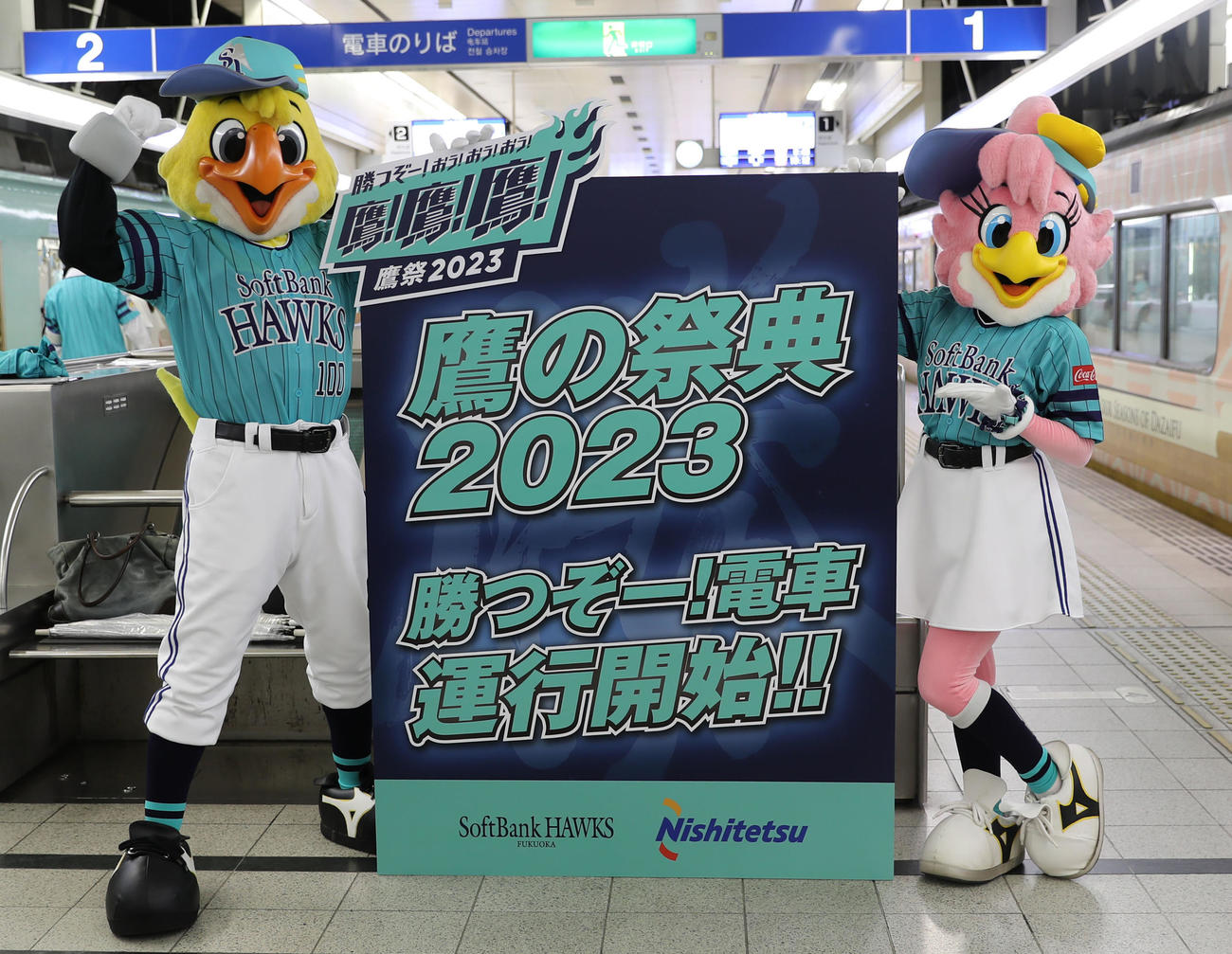 鷹の祭典2023特別デザインの西鉄ラッピング電車「勝つぞー！電車」運行開始パネルを手に、ポーズを決めるハリーホーク(左)とハニーホーク(撮影・冨田成美)