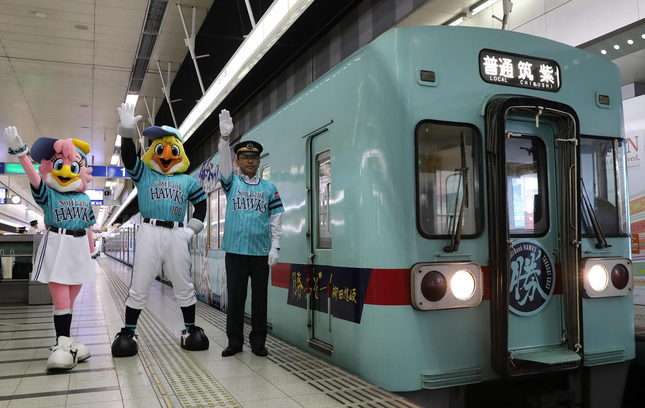 鷹の祭典2023特別デザインの西鉄ラッピング電車「勝つぞー！電車」は野口駅長(右)の合図で出発する、一緒に手を挙げるハリーホーク(中央)とハニーホーク(撮影・冨田成美)