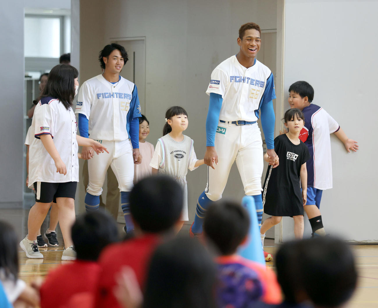 北広島西部小学校を訪れ児童たちにエスコートされながら入場する日本ハム細川（左後方）と万波（撮影・佐藤翔太）