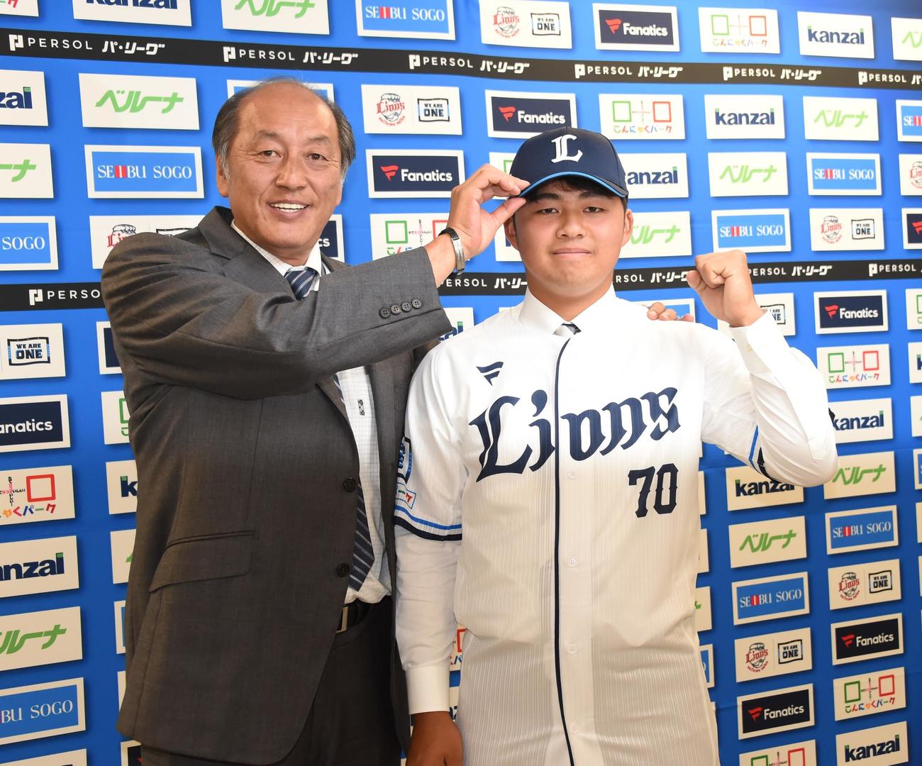 支配下選手契約を結んだ西武豆田（右）は渡辺GMから帽子をかぶせてもらいガッツポーズで健闘を誓う（撮影・鈴木正章）