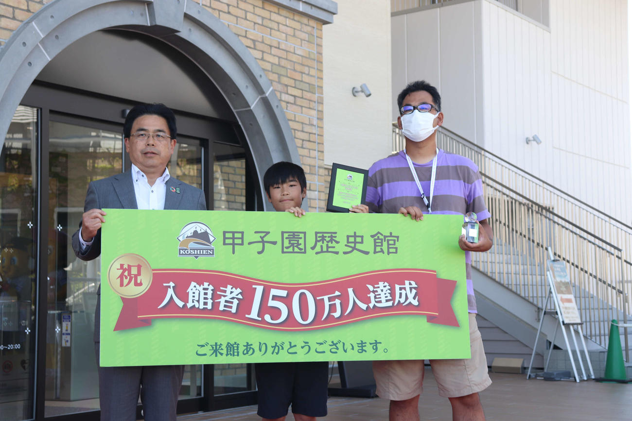 甲子園歴史館の入館者150万人達成セレモニーで記念撮影する、小岩隼真くん（中央）と父陽平さん（右）。写真左は谷本修館長