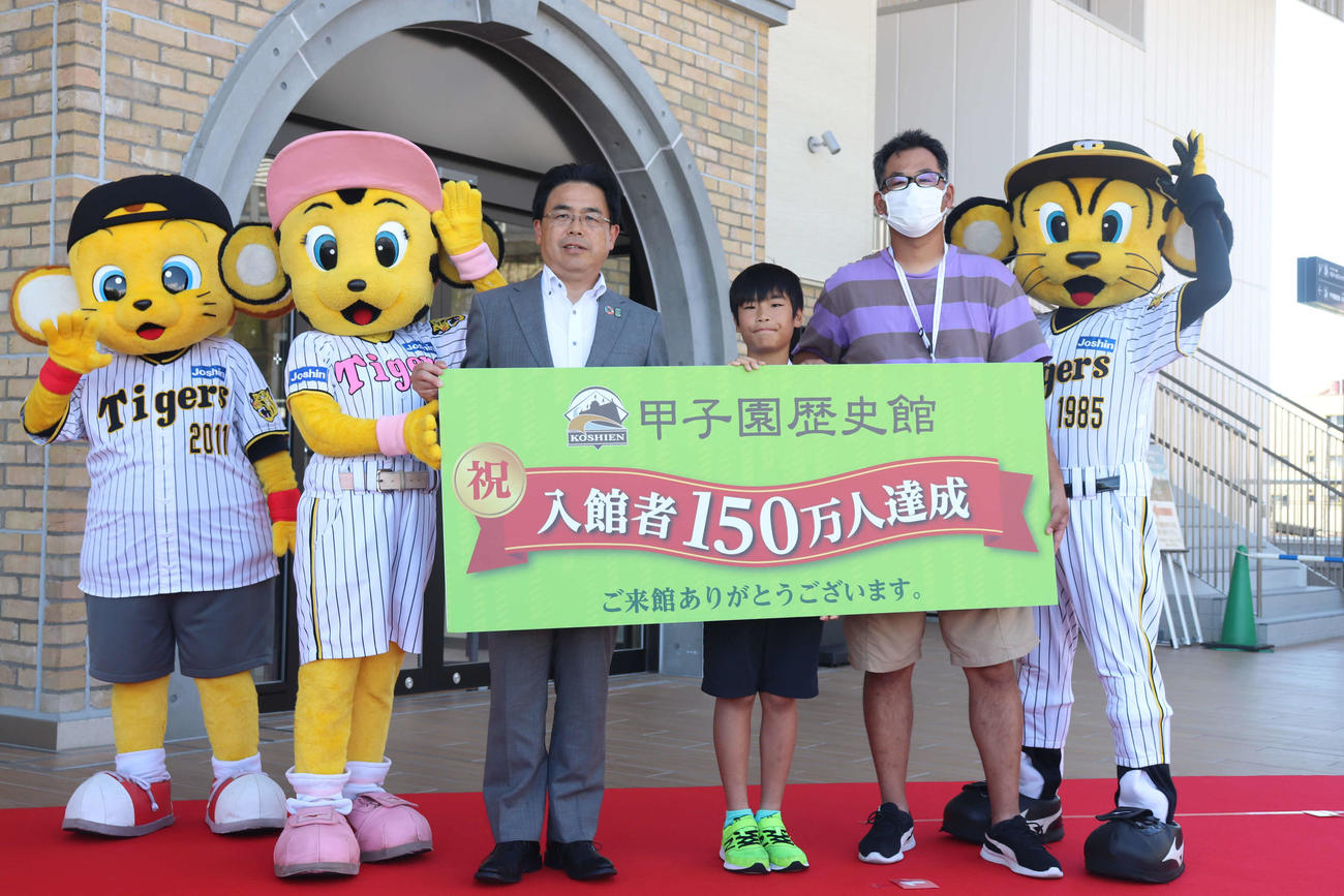 甲子園歴史館の入館者150万人達成セレモニーでマスコットらと記念撮影する小岩隼真くん（中央）と父陽平さん（右）。写真左は谷本修館長