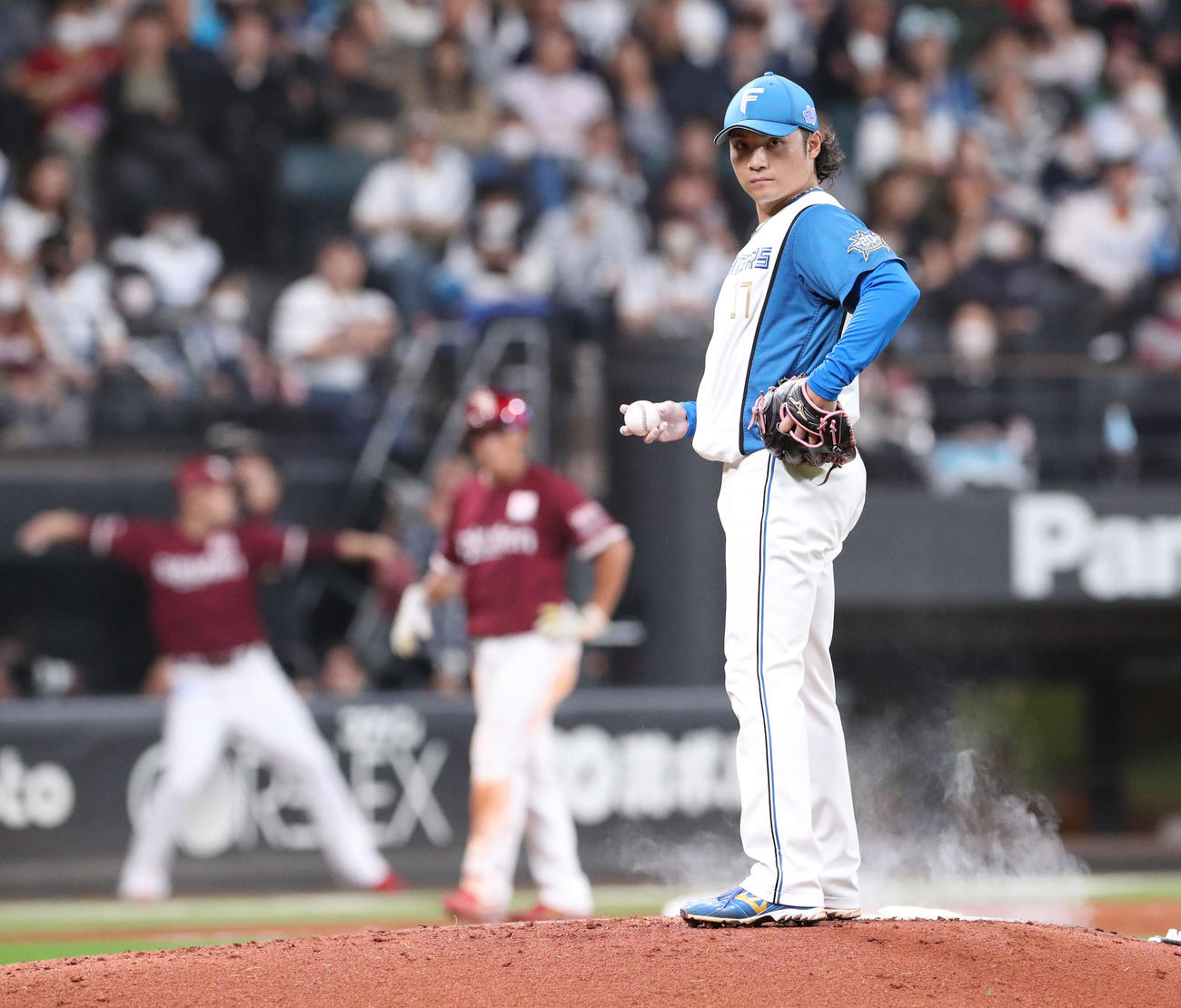 日本ハム対楽天　マウンドでロジンをつける日本ハム伊藤。左後方はキャッチボールをする楽天田中将（撮影・佐藤翔太）
