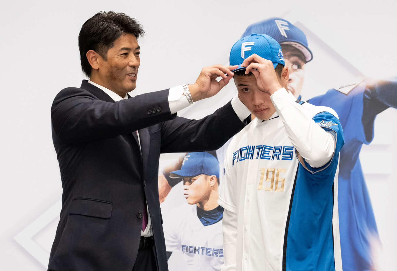 入団会見で孫易磊（右）に帽子を被せる日本ハム稲葉GM（球団提供）