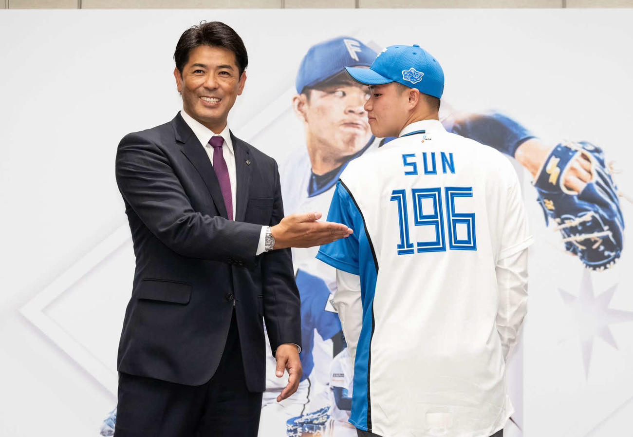 日本ハムの入団会見でポーズを取る孫易磊（右）と稲葉GM（球団提供）