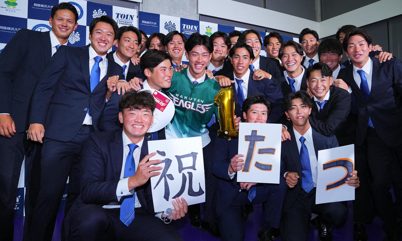 楽天から1位指名を受けた桐蔭横浜大・古謝（中央）はチームメートと笑顔で写真に納まる（撮影・垰建太）