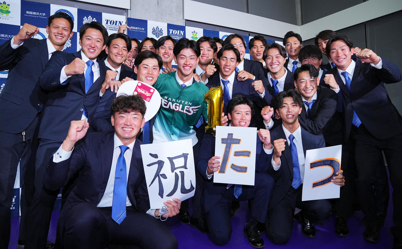 楽天から1位指名を受けた桐蔭横浜大・古謝（中央）はチームメートと笑顔で写真に納まる（撮影・垰建太）