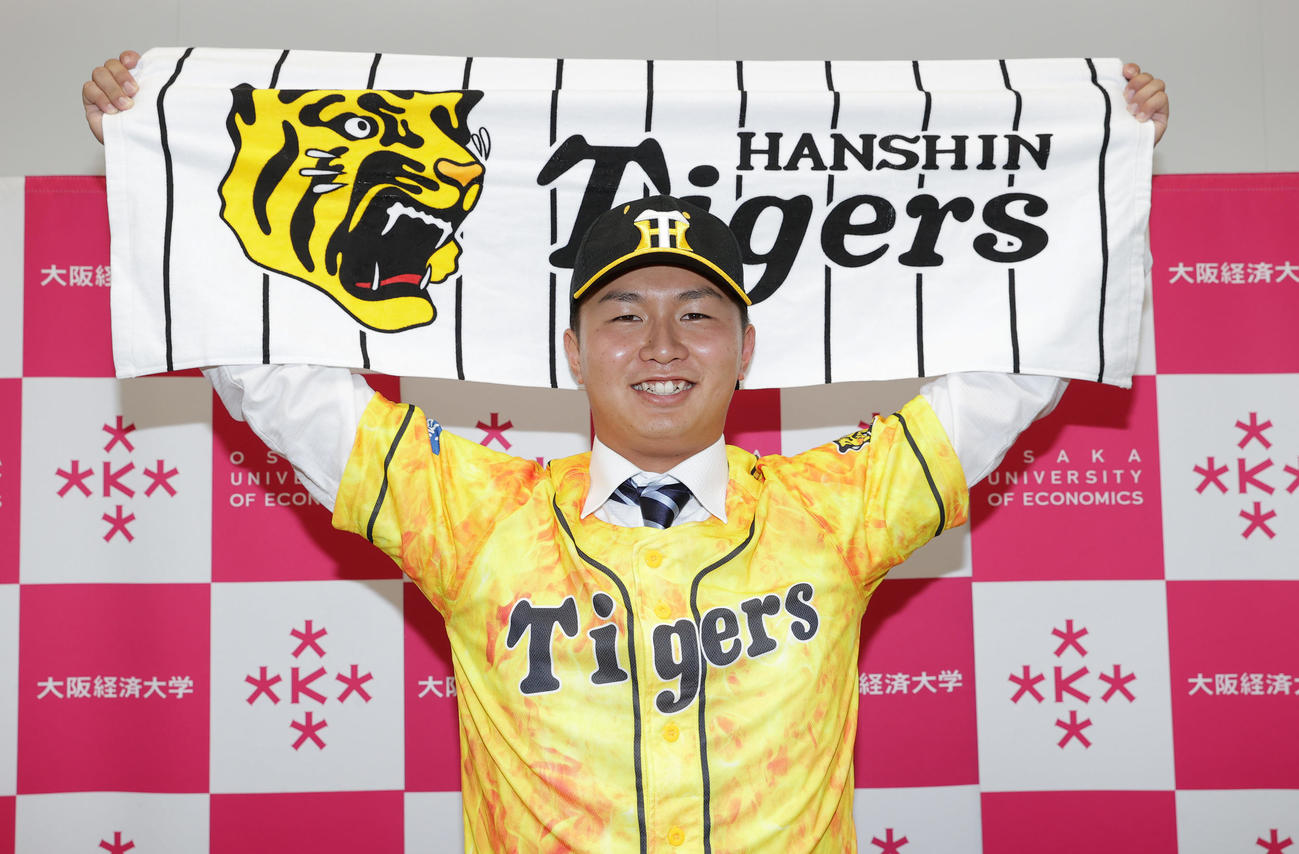 阪神から6位指名を受け、笑顔でポーズを決める大経大・津田（撮影・前田充）