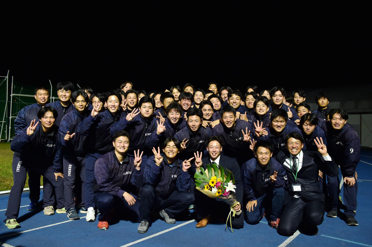 野球部員と集合写真に納まり、花束を持ちながら笑顔を見せる仙台大・辻本（前列左から4人目）（撮影・相沢孔志）