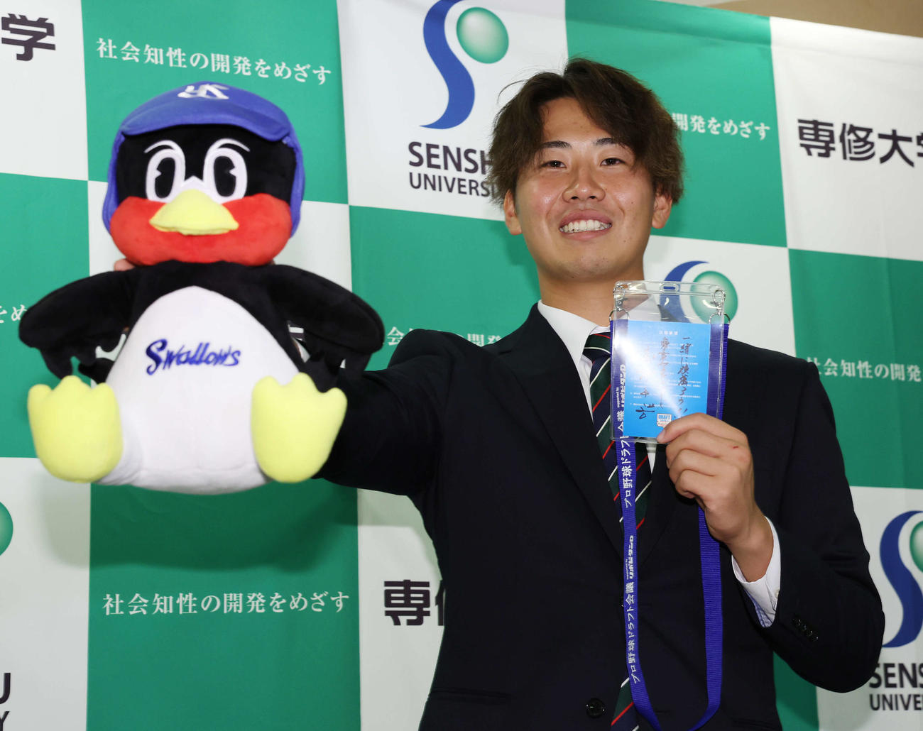 ヤクルト高津監督からのメッセージとつば九郎を手に笑顔を見せる1位指名の専大・西舘（撮影・宮地輝）