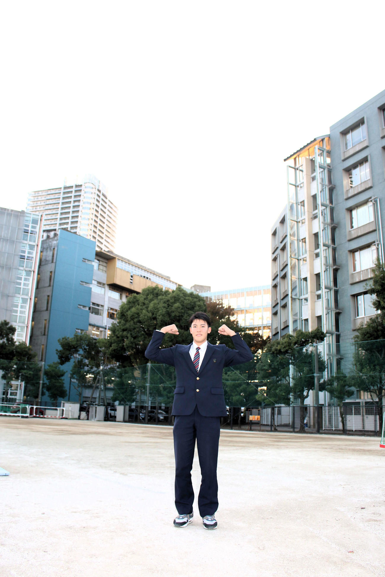 指名あいさつを受けて校舎をバックにポーズを取るロッテのドラフト4位幕張総合・早坂響投手（撮影・木下大輔）
