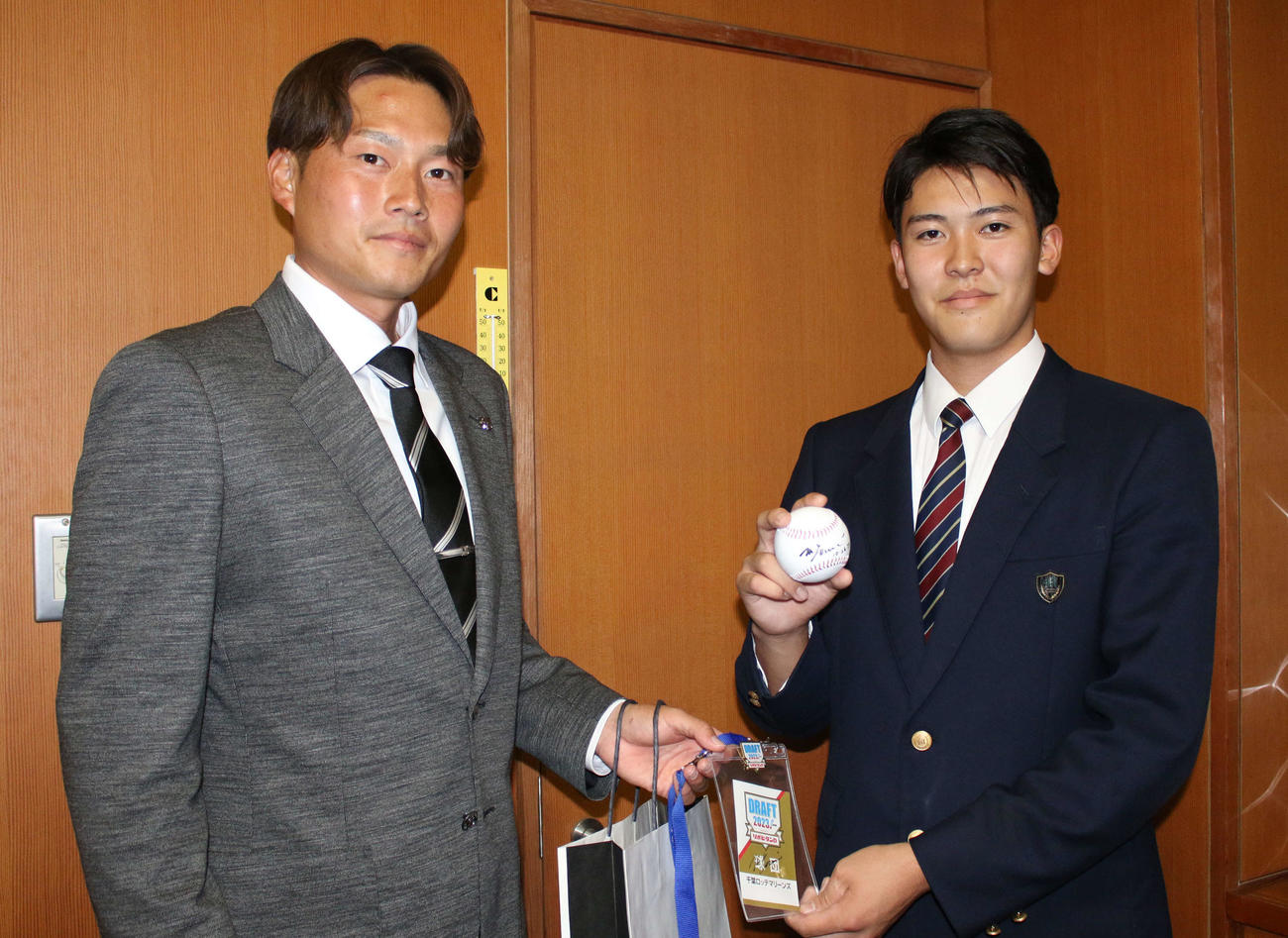 担当の有吉優樹スカウト（左）から吉井理人監督のサイン入りドラフト会場のIDなどを受け取ったロッテのドラフト4位幕張総合・早坂響投手（撮影・木下大輔）