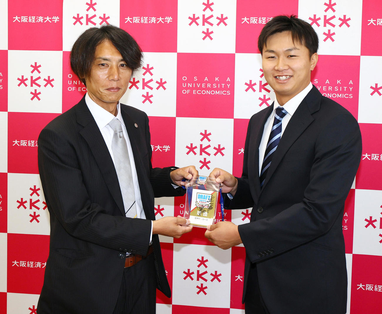 大経大・津田（右）は阪神渡辺スカウトから岡田監督のサイン入りドラフト入場証を受け取り笑顔を見せる（撮影・上山淳一）