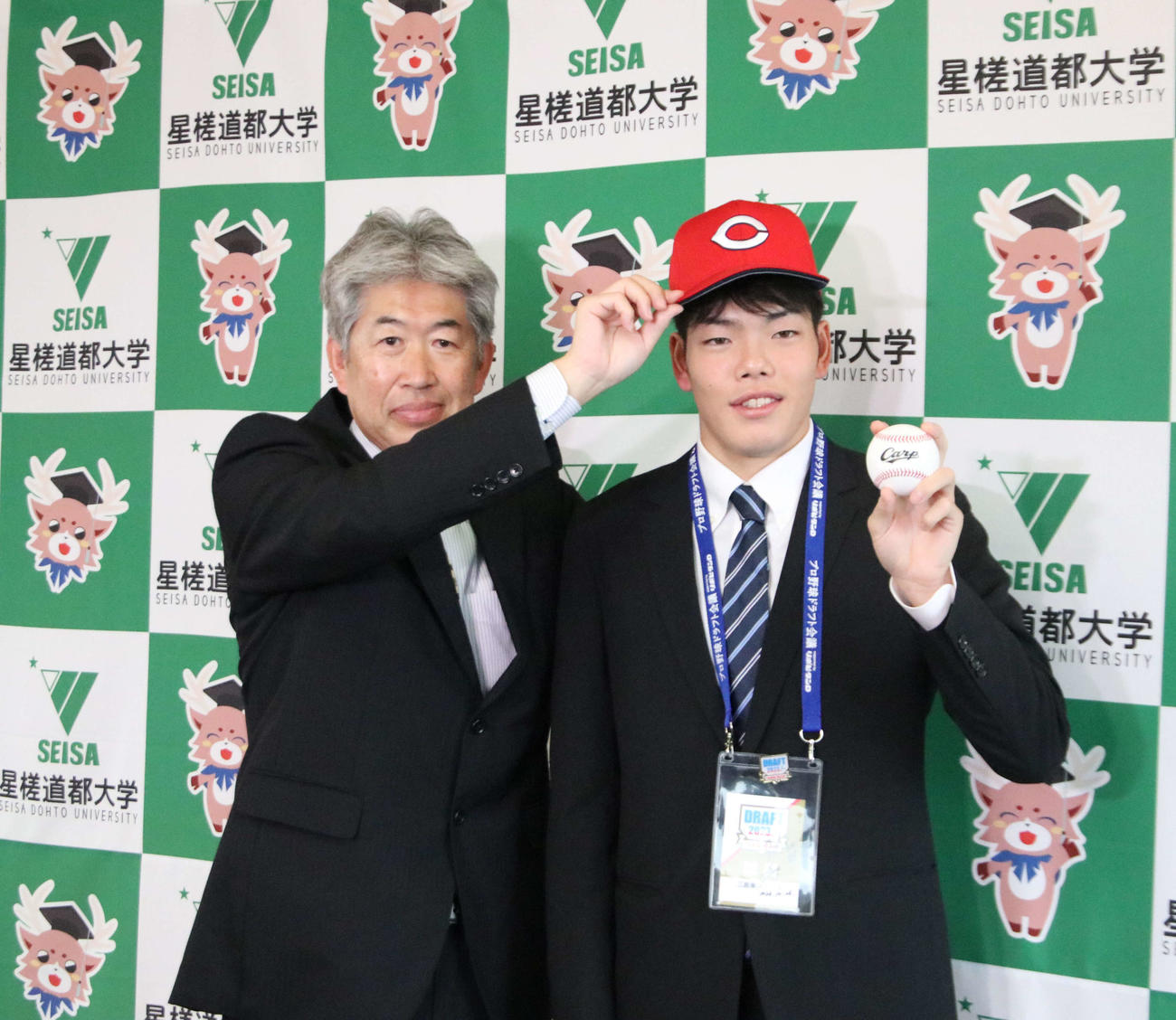 近藤スカウト（左）から帽子をかぶせてもらい、笑顔をみせる広島ドラフト3位の星槎道都大・滝田（撮影・山崎純一）