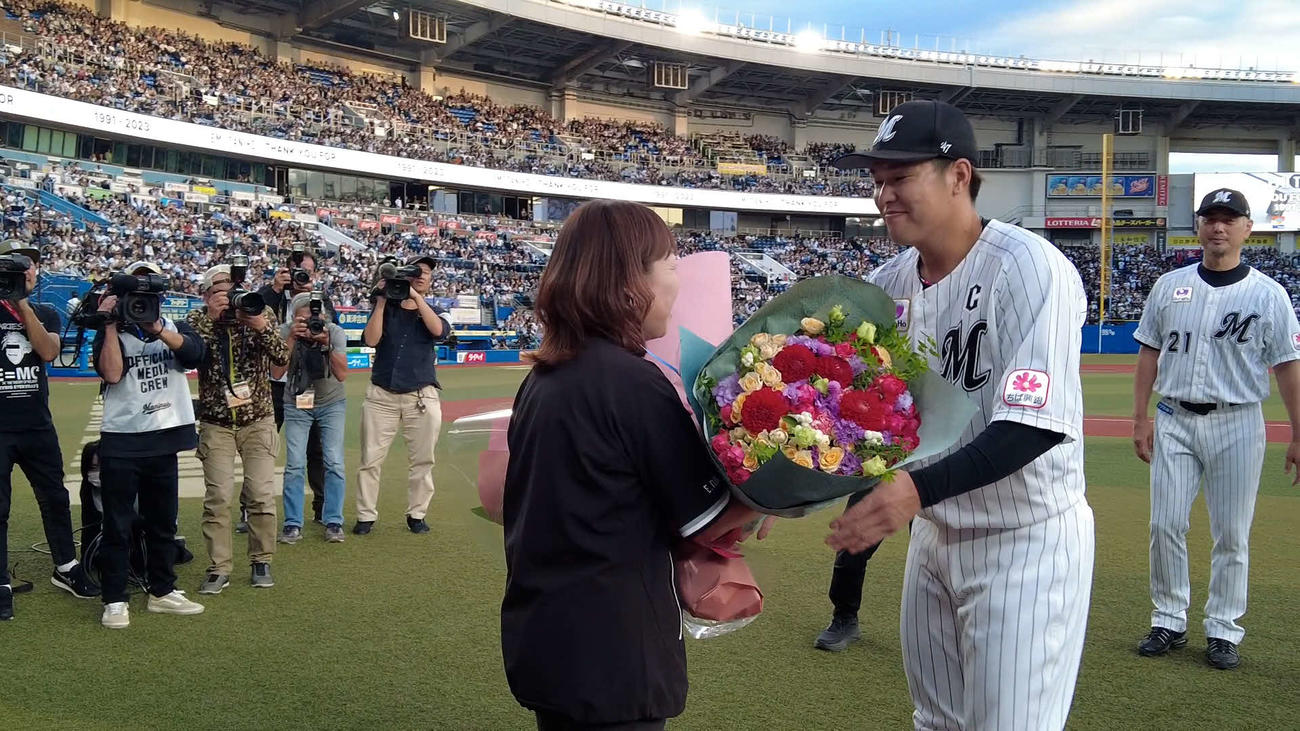 10月7日のオリックス戦でロッテ中村奨から花束が贈られる、場内アナウンスの谷保さん（球団提供）