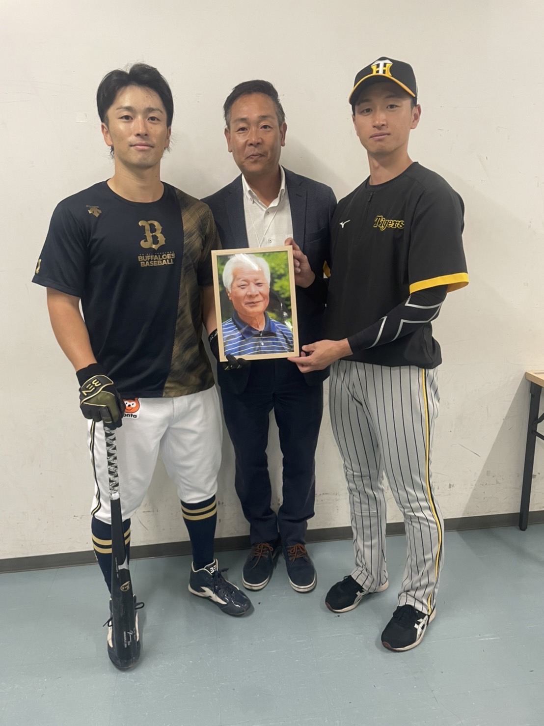 10月28日、日本シリーズ開幕前に昨年11月に亡くなったヤナセ社の社長・柳瀬隆臣さんの遺影と写真に納まる阪神近本（右）、オリックス福田（左）、ヤナセ社の北村さん（ヤナセ社提供）