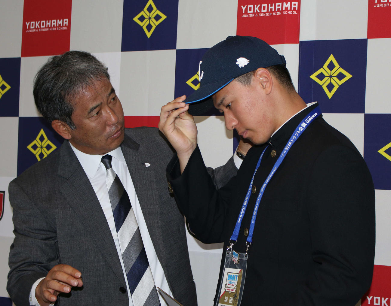 西武から指名あいさつ後に西武潮崎哲也球団本部編成グループディレクター（左）から帽子を被らせてもらうドラフト3位の横浜・杉山遥希投手（撮影・木下大輔）