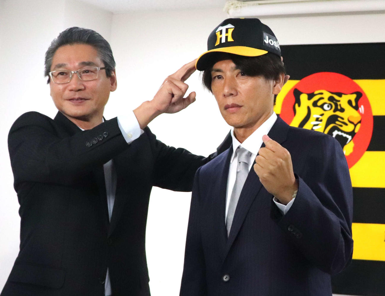 阪神2軍投手コーチに就任した渡辺亮氏は、嶌村球団本部長に帽子をかぶせてもらう（撮影・中島麗）