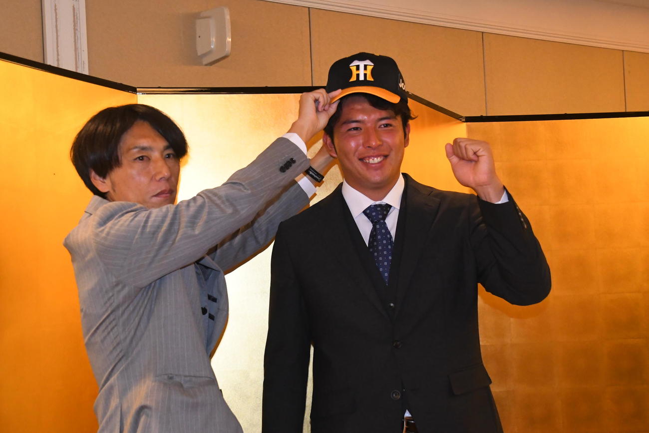 渡辺スカウト（左）に帽子をかぶせてもらう阪神ドラフト2位の椎葉（撮影・中野椋）