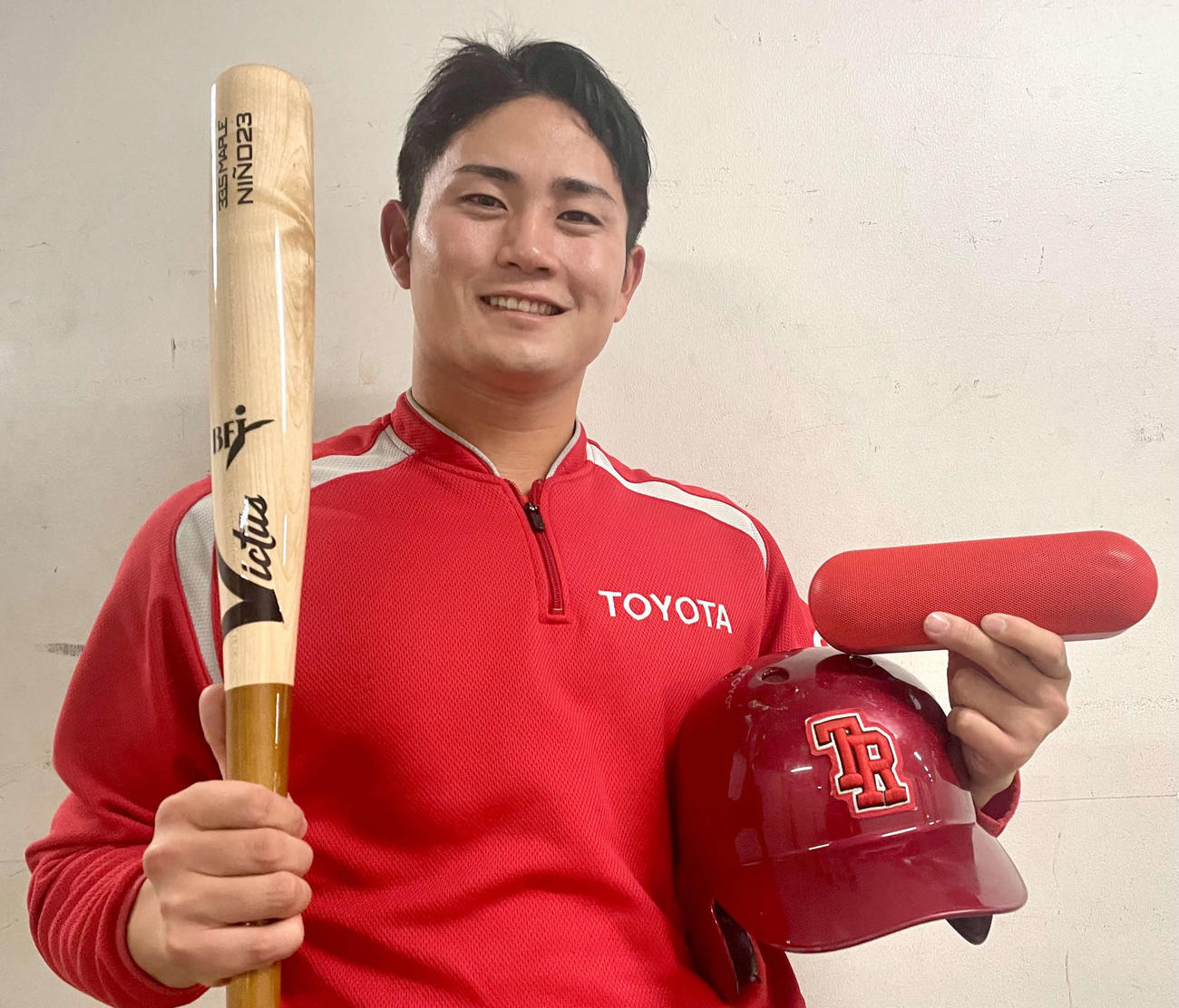 バットとヘルメットとともに、試合前のベンチ裏の声出しで使用するワイヤレススピーカーを持つ、トヨタ自動車の高橋（撮影・中島麗）