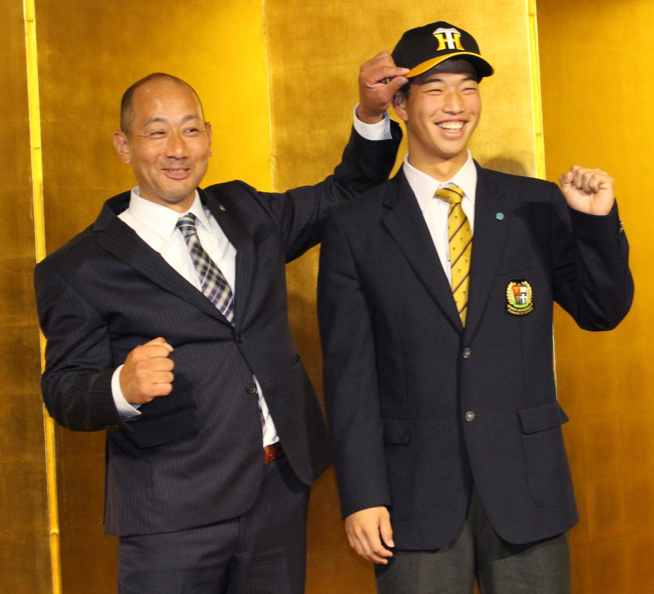 仮契約交渉を終え、前田忠節スカウトから帽子をかぶせてもらう阪神4位指名の東海大熊本星翔の百崎蒼生内野手（右）（撮影・菊川光一）