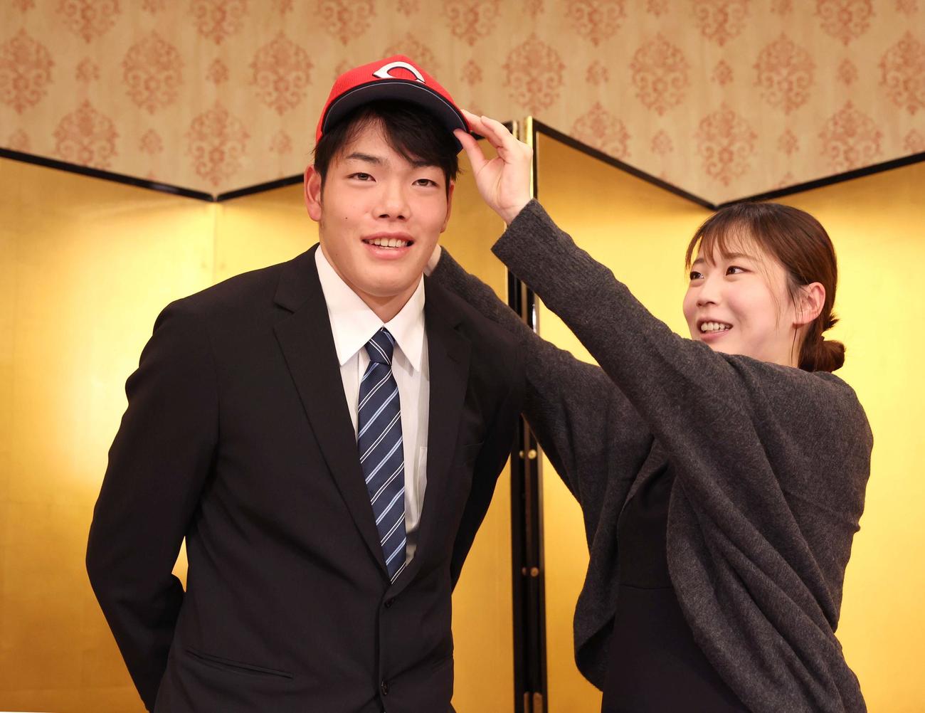 広島と仮契約を終え姉優衣さん（右）から帽子をかぶせてもらう滝田（撮影・黒川智章）