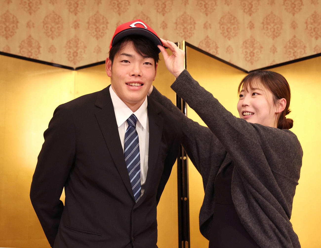 広島と仮契約を終え姉優衣さん（右）から帽子をかぶせてもらう滝田（撮影・黒川智章）