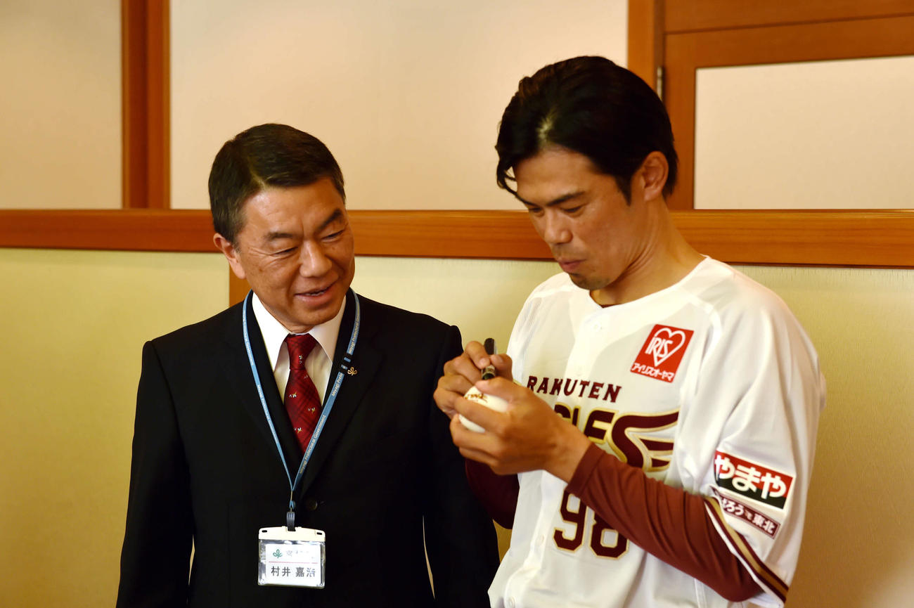 村井知事（左）の前でボールにサインを書く楽天今江監督