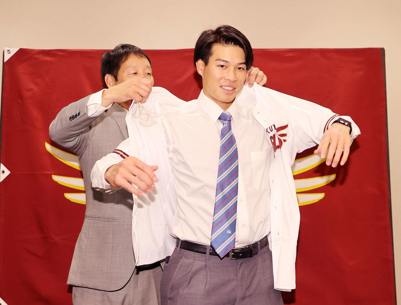 部坂スカウト（左）にユニホームを着せてもらう楽天ドラフト6位の青学大・中島（撮影・鈴木正人）