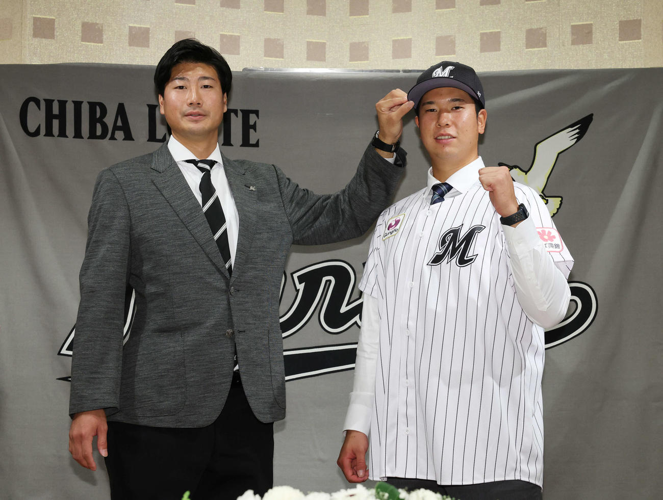 契約終え、ロッテ松田スカウト（左）に帽子をかぶせてもらい、ガッツポーズするドラフト1位の明大・上田（撮影・宮地輝）