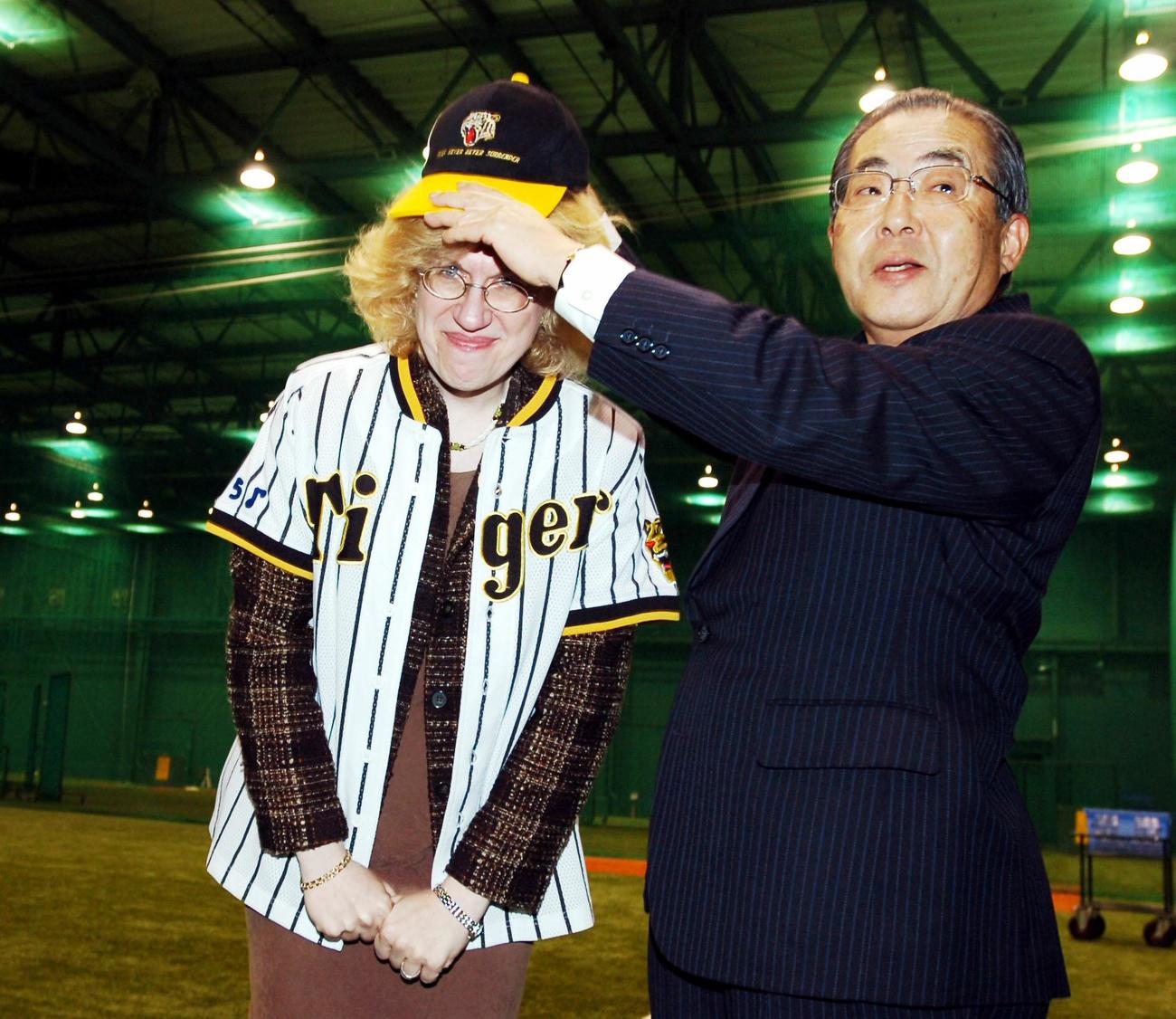 持参のユニホームを着用し、甲子園球場の室内練習場で阪神・宮崎恒彰オーナー（右）に帽子をかぶせてもらうカナダ・バンクーバー在住で自称「トラキチ」、ピアニストでブリティッシュ・コロンビア大学のサラ・ブュクナー教授(2007年12月19日撮影)