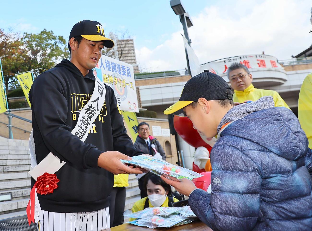 1日人権擁護委員を勤めた岡留（左）は集まった市民に啓発物品を手渡す（撮影・上田博志）
