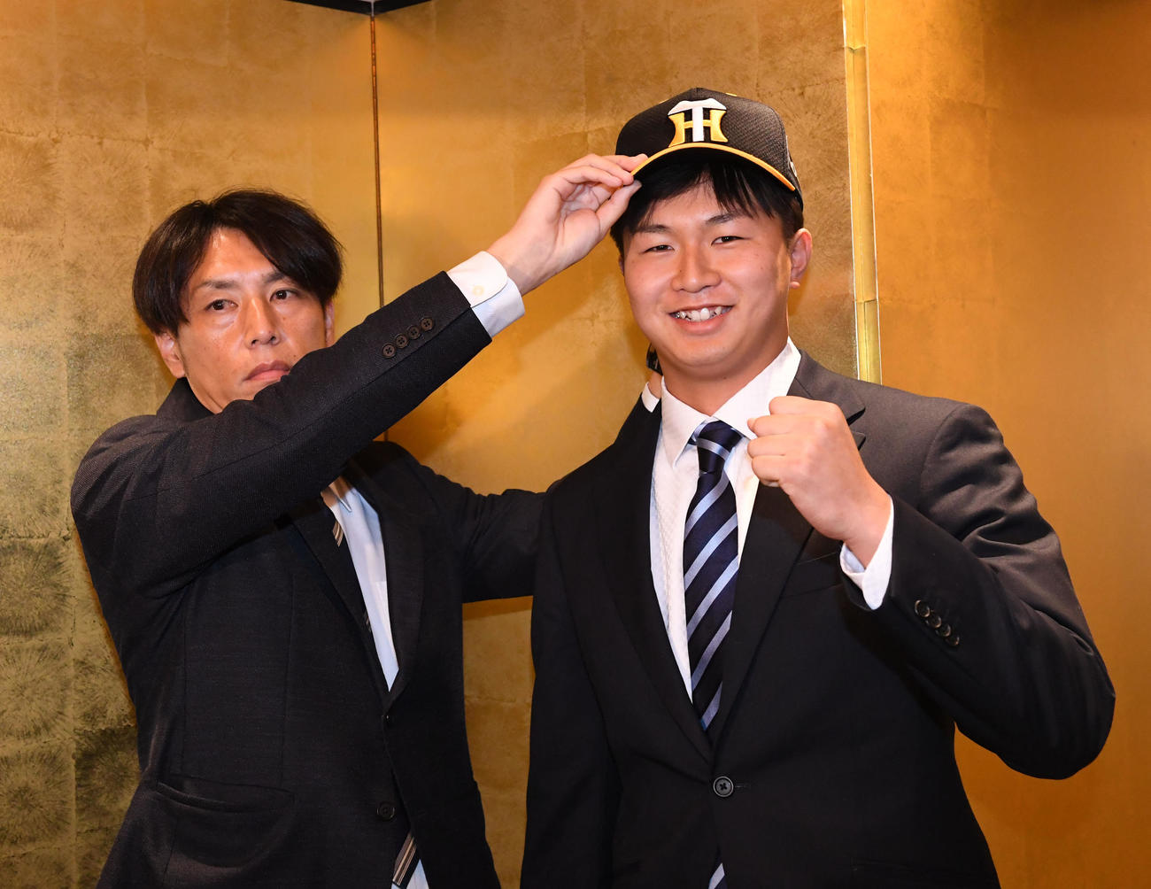 阪神と仮契約を結んだ津田（右）は、渡辺スカウトから帽子をかぶせてもらい笑顔を見せる（撮影・前岡正明）