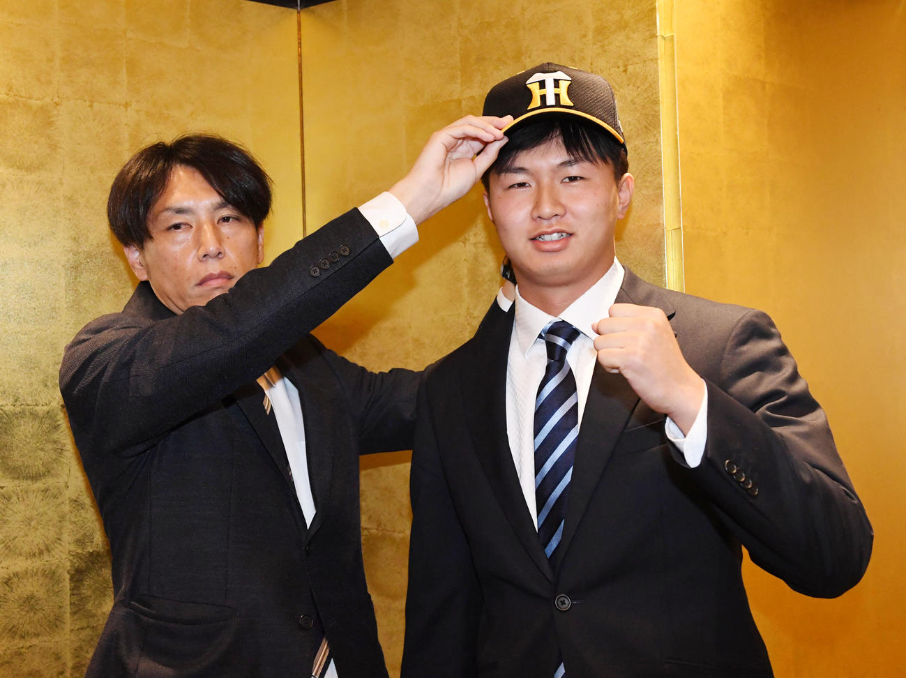 阪神と仮契約を結んだ津田（右）は渡辺スカウトから帽子をかぶせてもらい笑顔を見せる（撮影・前岡正明）