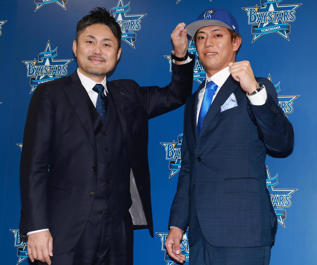 入団会見で萩原チーム統括本部長（左）から帽子をかぶせられるDeNA九鬼（撮影・野上伸悟）
