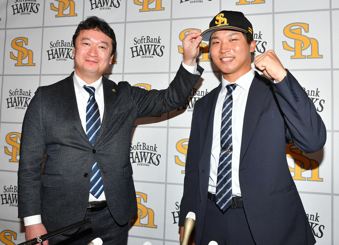 現役ドラフトでソフトバンクに入団した長谷川（右）は、三笠GMから帽子をかぶせてもらいガッツポーズする（撮影・岩下翔太）