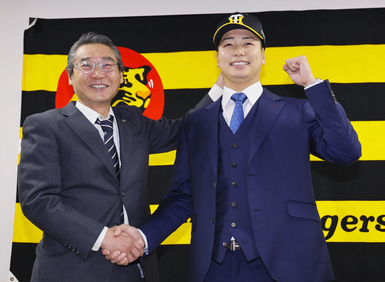 現役ドラフトで阪神に入団し、嶌村球団本部長（左）と握手を交わす漆原（撮影・藤尾明華）