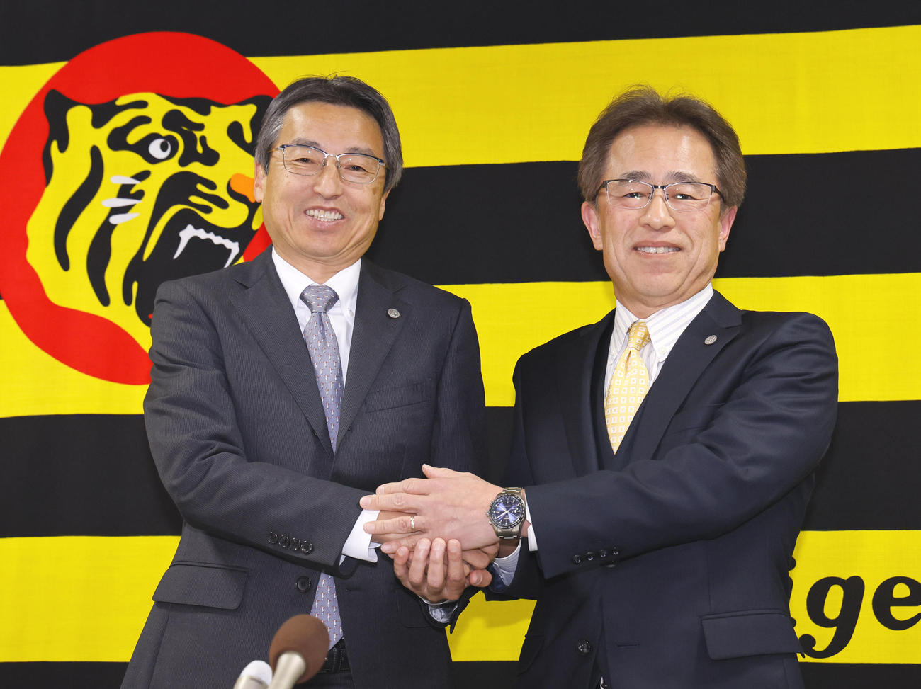 記者会見を終え握手を交わす阪神の百北球団社長（左）と、次期社長に就任する粟井副社長（撮影・藤尾明華）