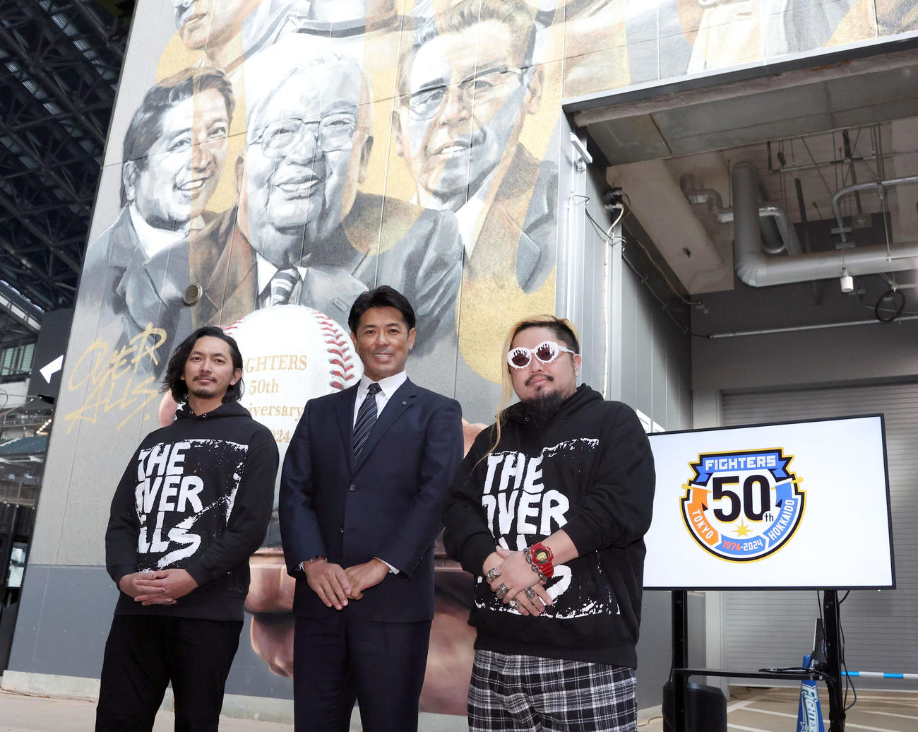 日本ハム球団創立50周年を記念し描かれた新ウォールアート背にフォトセッションをする稲葉2軍監督（中央）と描いた「OVER ALLs」の二人（撮影・佐藤翔太）